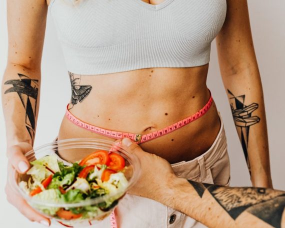 Fit woman measuring waist while holding a healthy salad bowl